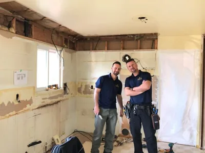 Two Golden Leaf electricians in branded shirts on a kitchen rough-in, cabinetry stripped back and vapour barrier up.